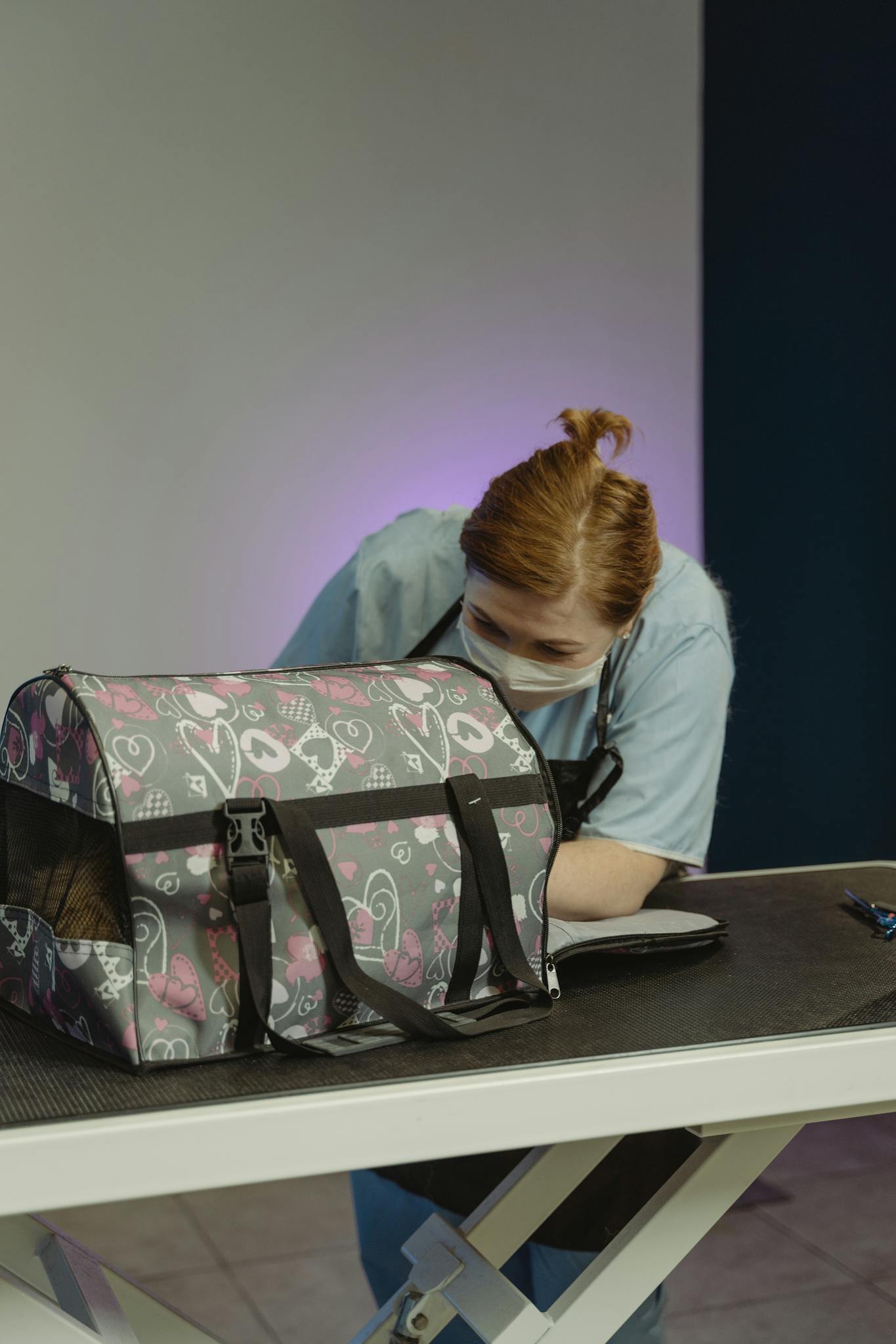 Professional pet groomer tending to a pet carrier on a grooming table.